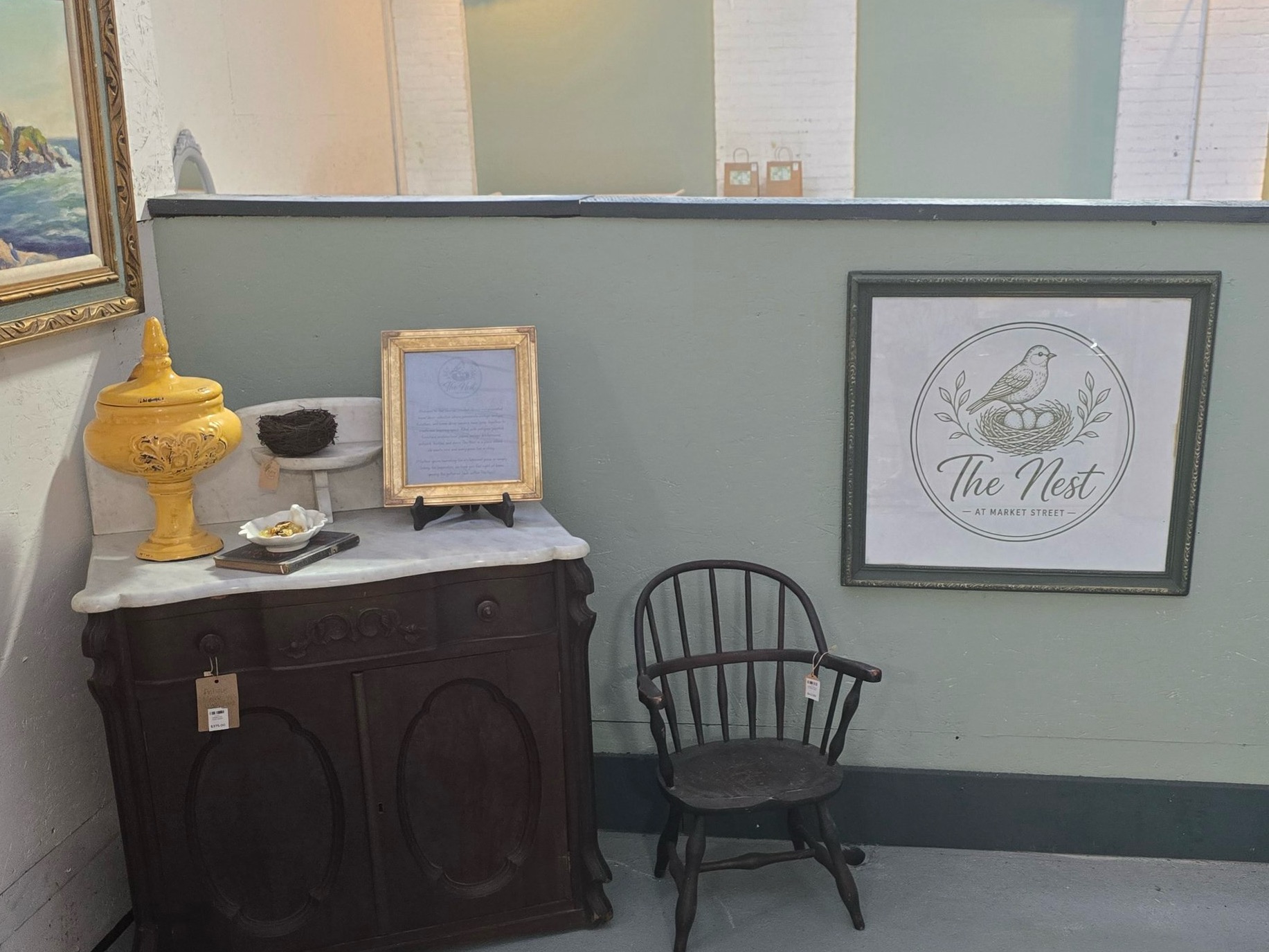 A corner of The Nest with an antique marble-top cabinet, a Windsor chair, and the framed The Nest at Market Street sign.